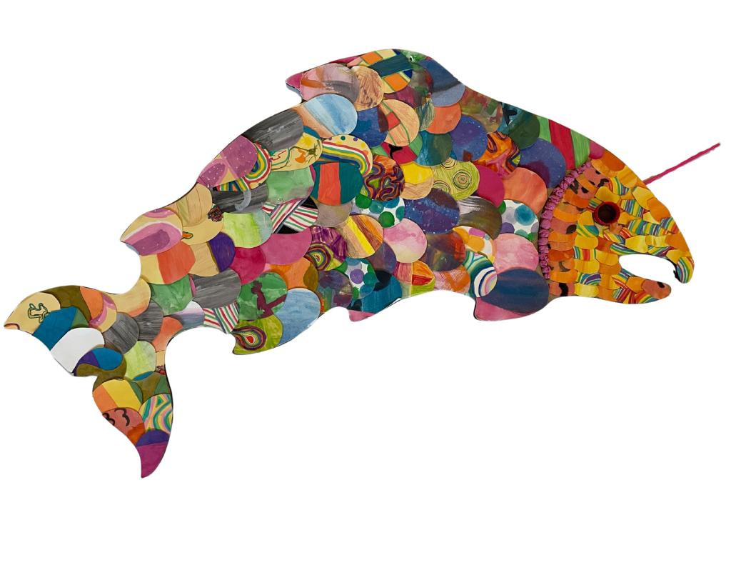 Salmon artwork- a salmon decorated with various paper scales decorated by students, complete with a bottle cap eye and chopstick unicorn horn
