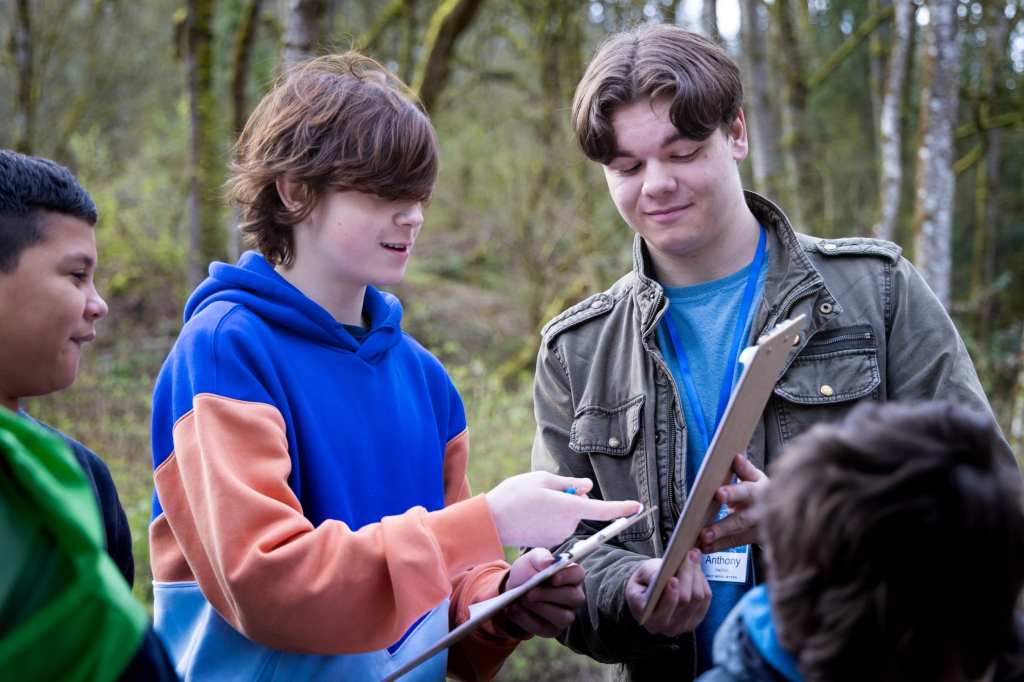 8/19 A high school intern helps elementary school students find items on a nature Bingo card.