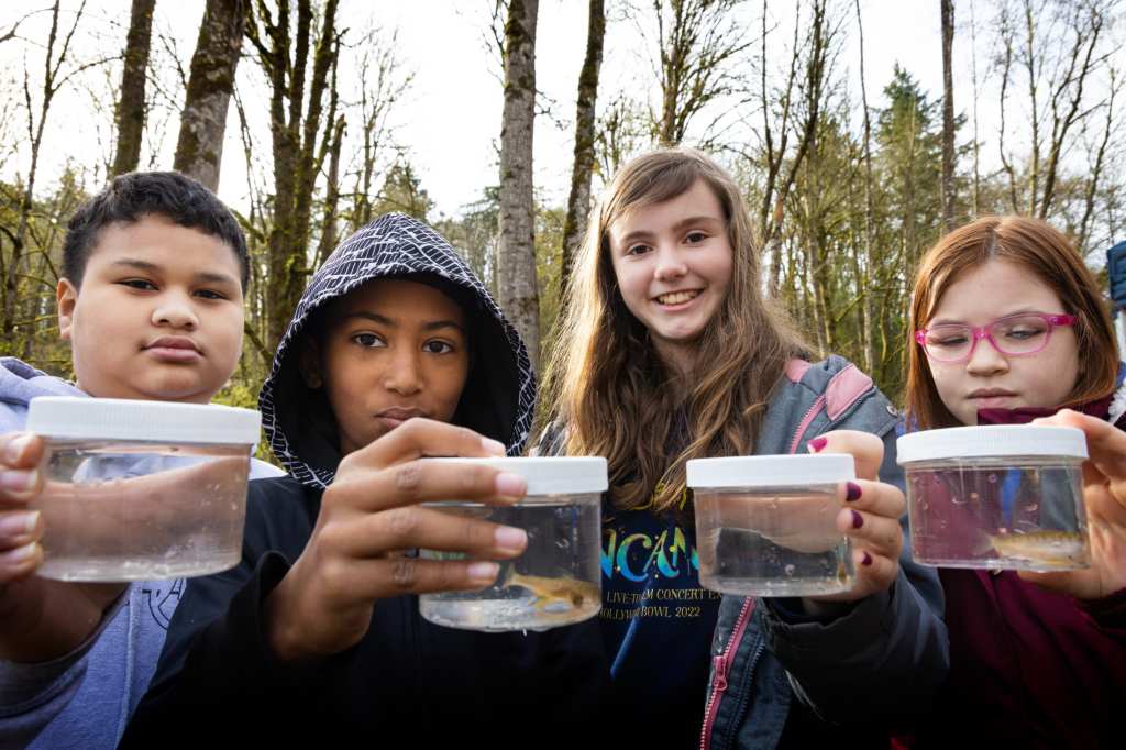 8/19 Four students display jars containing the salmon fry they are about to release.