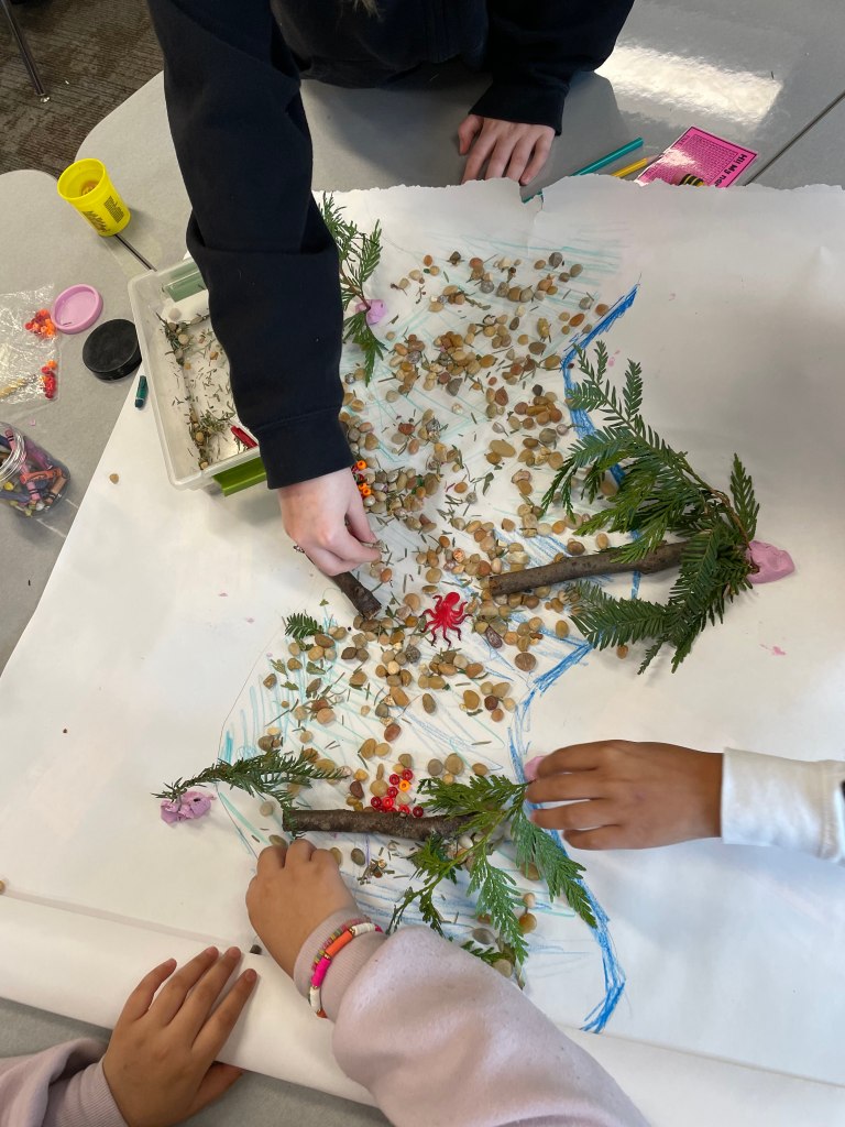 Students working on a model of salmon habitat using gravel, plant clippings, twigs, playdoh, and toys